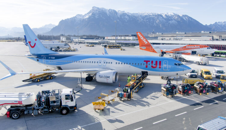 Ein TUI-Flugzeug auf dem Rollfeld des Flughafens, Gepäck wird verladen, im Hintergrund sind Berge und andere Flugzeuge zu sehen.