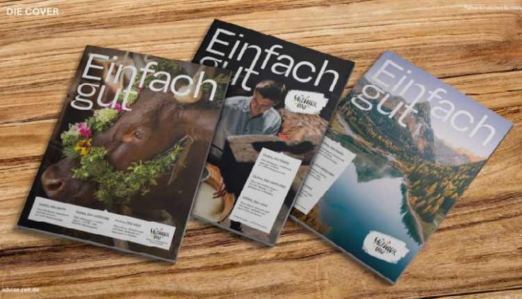 Drei Ausgaben der Zeitschrift „Einfach gut“ auf einem Holztisch, auf deren Titelseiten eine Kuh, ein Koch und ein See abgebildet sind.
