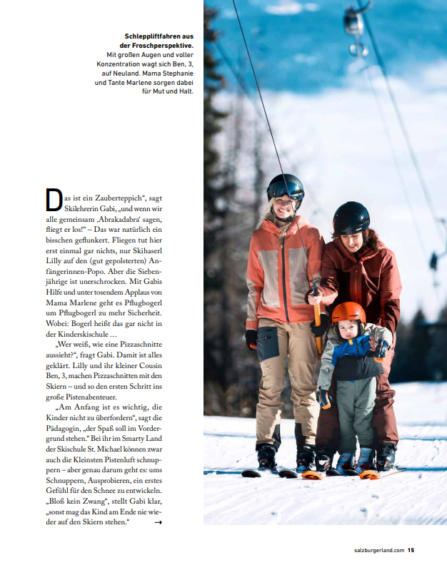Eine dreiköpfige Familie in Winterkleidung lächelt auf einem verschneiten Hang mit Bäumen und blauem Himmel – zu sehen im Magazin „Jederzeit“.