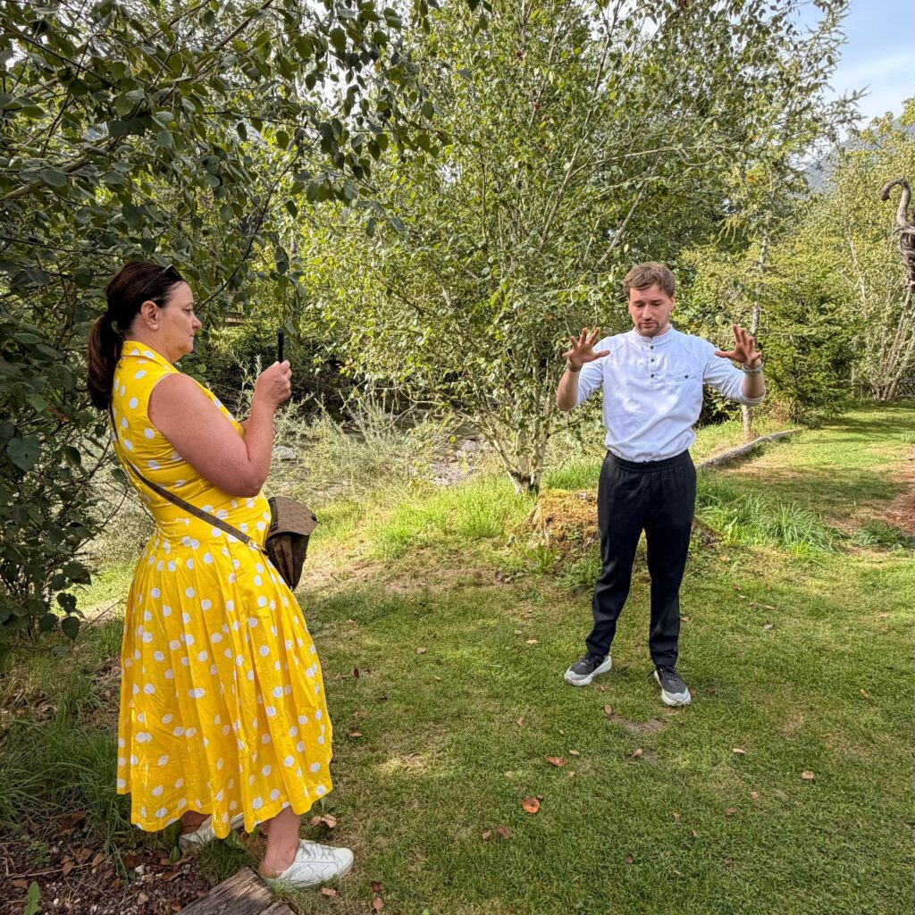 Eine Frau in einem gelben Kleid fotografiert einen Mann vor der malerischen, grasbewachsenen Kulisse von „SalzburgerLand-Medienspecials“.