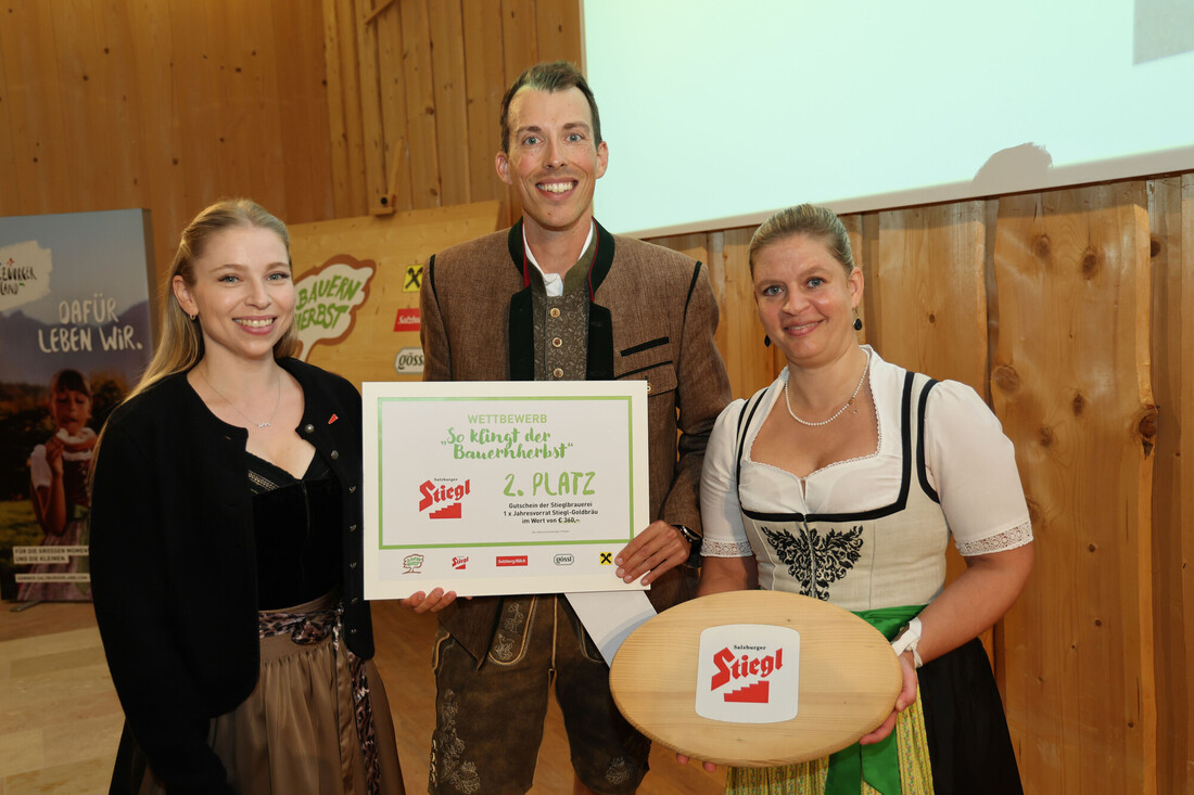 Drei Personen in traditioneller österreichischer Tracht halten eine Urkunde für den zweiten Platz bei einem Stiegl-Bierwettbewerb in den Händen.