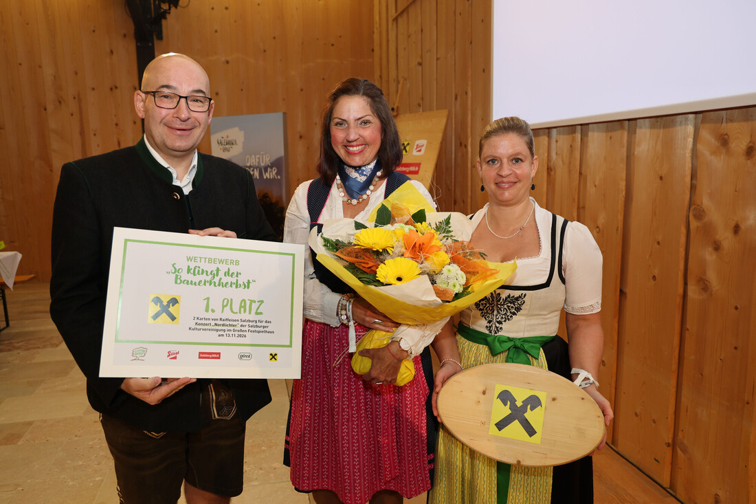 Drei Personen in traditioneller österreichischer Tracht, die eine Urkunde für den ersten Platz und einen Blumenstrauß in den Händen halten.