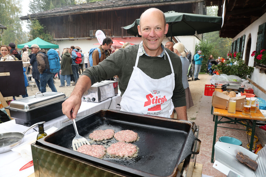 Ein Mann, der eine Schürze mit Markenlogo trägt, wendet bei einer Veranstaltung im Freien Burger-Patties auf einem Flachgrill.