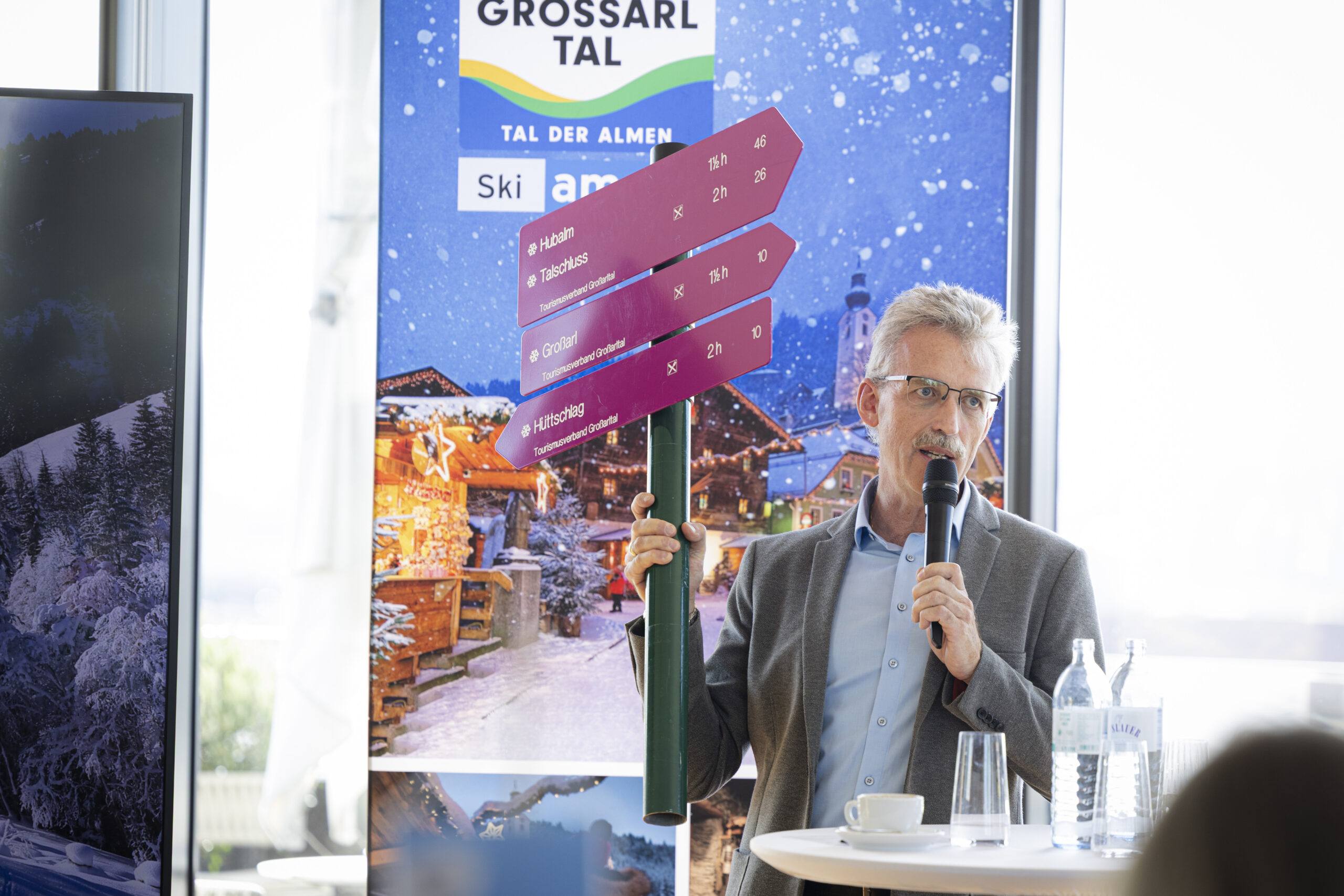 Ein Mann spricht in ein Mikrofon, während er ein Schild in der Hand hält, auf dem die Ziele im österreichischen Großarltal angegeben sind.
