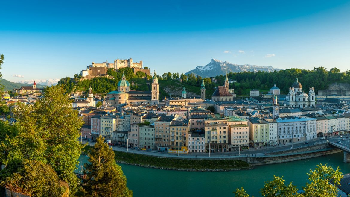 Panoramablick auf Salzburg, Österreich, mit bunten Gebäuden, einer Festung und Bergen im Hintergrund.