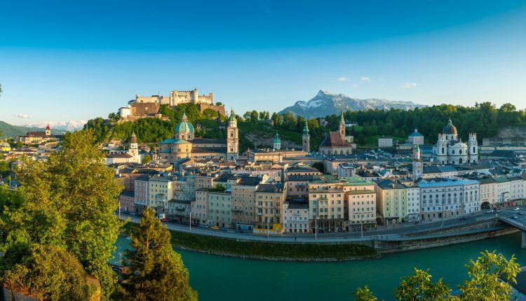 Panoramablick auf Salzburg, Österreich, mit bunten Gebäuden, einer Festung und Bergen im Hintergrund.